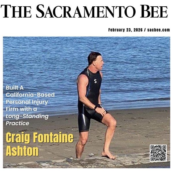 A man in a wetsuit stands on a sandy beach near the water, looking to the side. The Sacramento Bee masthead and headline text about Craig Fontaine Ashton are overlaid on the image, dated February 23, 2026.